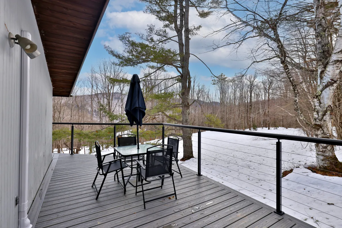 An inviting outdoor dining area sits under an umbrella with a backdrop of trees and snow. The spacious table suggests the perfect spot for al fresco meals, stargazing, or simply relaxing together in the natural surroundings.