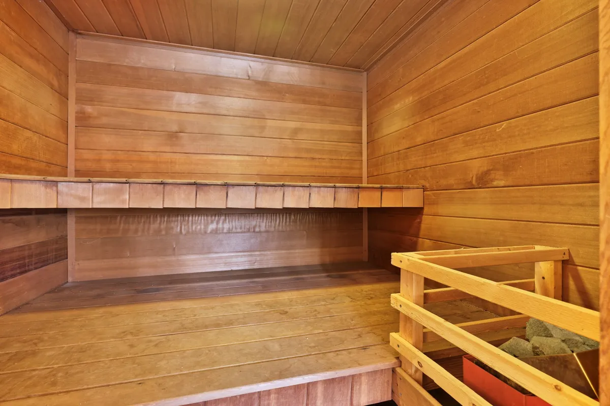 This image features a serene, wood-paneled sauna with classic wooden benches and a stone heater. The warm tones and simple design evoke a sense of relaxation and wellness, directly showcasing the private sauna amenity discussed in the section.