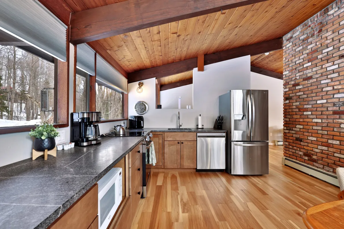 An open-concept kitchen adorned with stainless steel appliances, wooden ceiling beams, and a brick accent wall. The layout encourages family cooking and entertaining, with space for socializing and prepping meals together.