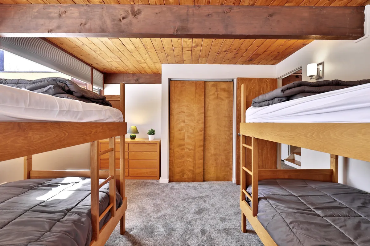 A cozy bedroom featuring sturdy bunk beds with wooden beams and a dresser. The inviting setup evokes childhood adventures and highlights the unique sleeping arrangement for families, with the ladder to the top bunk visible.