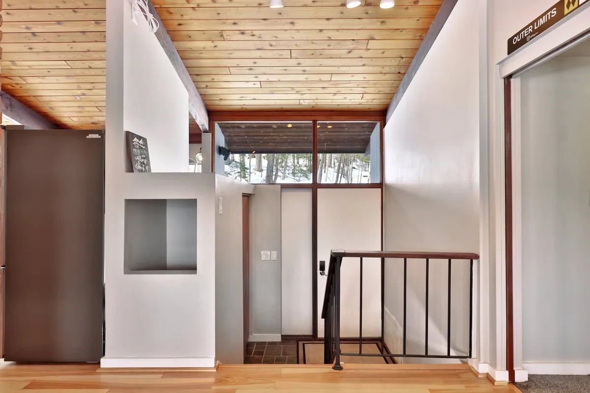 An inviting entryway with a staircase, expansive windows framing nature views, and a high wooden ceiling. The natural light and open sightlines connect the indoors to the outdoors, suggesting an easy transition between adventure and home comforts.