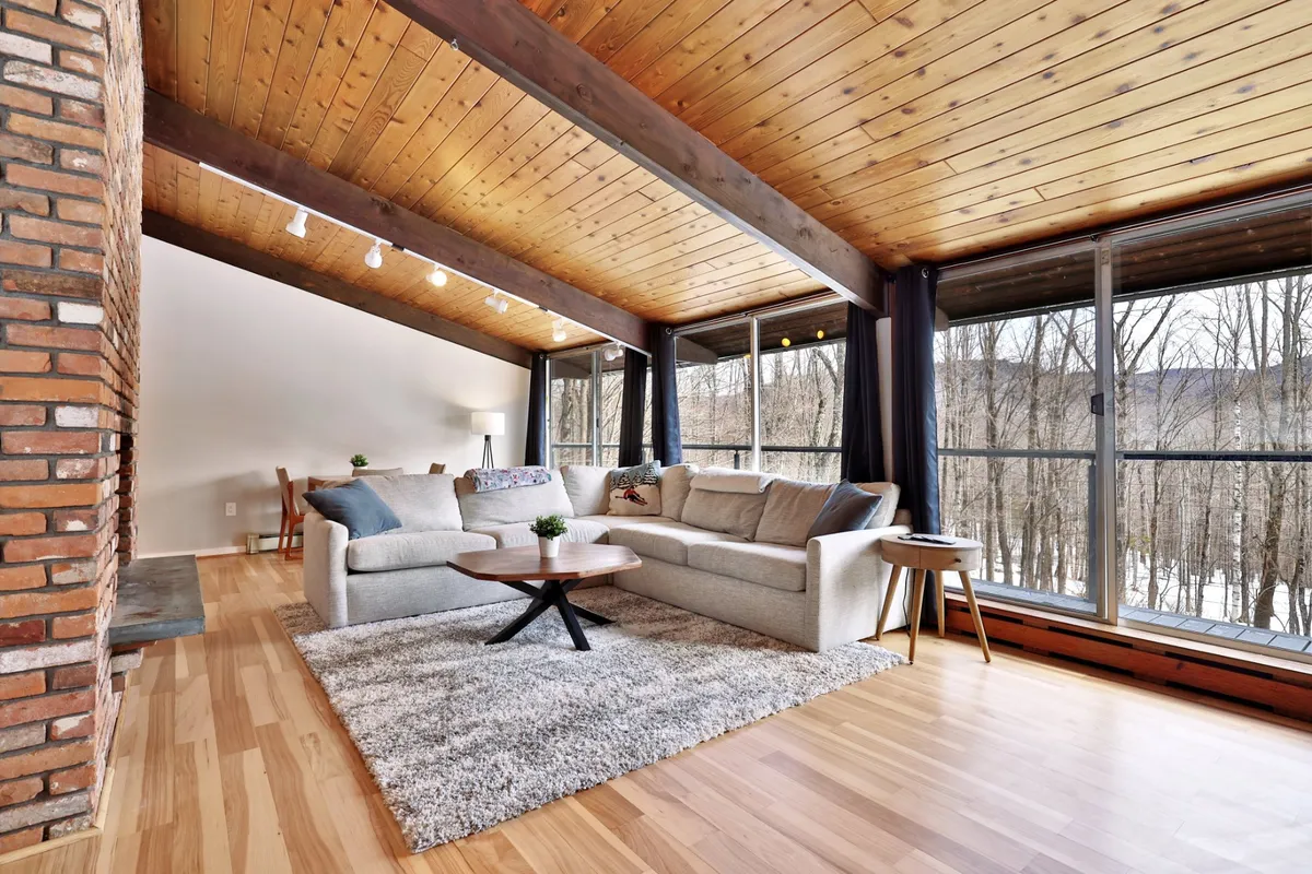 A cozy living room featuring a comfortable sofa, coffee table, large windows with views of the outdoors, and a classic brick wall. The space feels inviting and is ideal for socializing, sharing stories, or simply relaxing after a day on the mountain.
