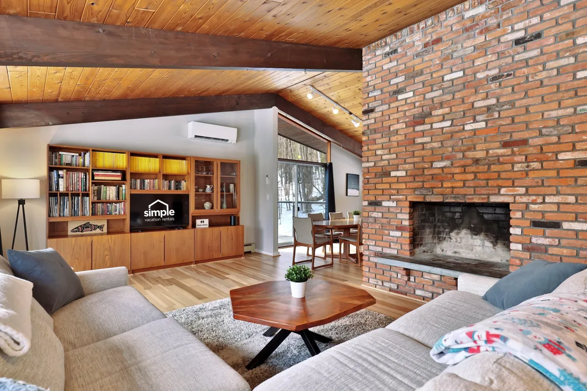 The hero image showcases a cozy interior living space featuring a glowing brick fireplace, rustic wooden ceiling beams, a welcoming coffee table, and a bookshelf—all arranged to create an inviting atmosphere perfect for relaxing or socializing.