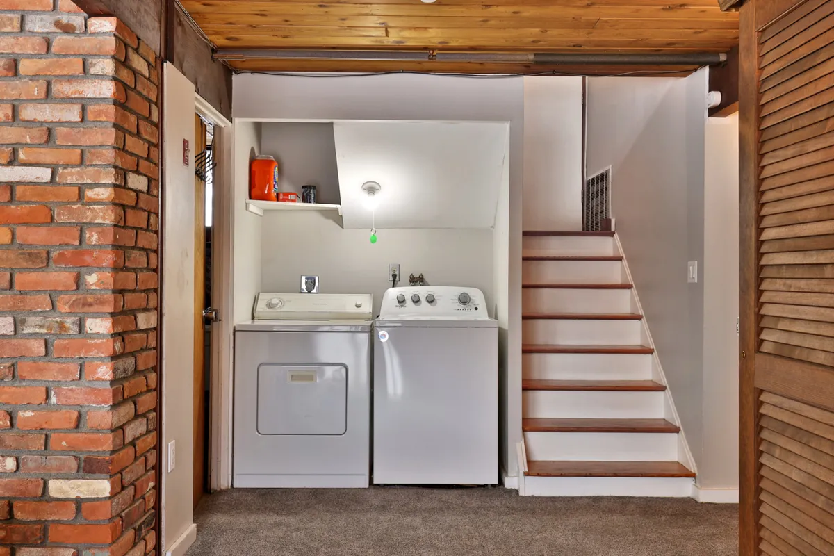 A practical, inviting utility area is depicted here, showcasing a modern washing machine and dryer, a sturdy staircase, and an exposed brick wall. The space feels organized and warm, signaling an emphasis on comfort and convenience for longer or active stays.